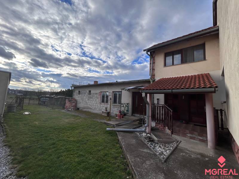 Rodinný dům v Zbechách s trávníkem, zahradou a kamenným chodníkem pod zamračenou oblohou.