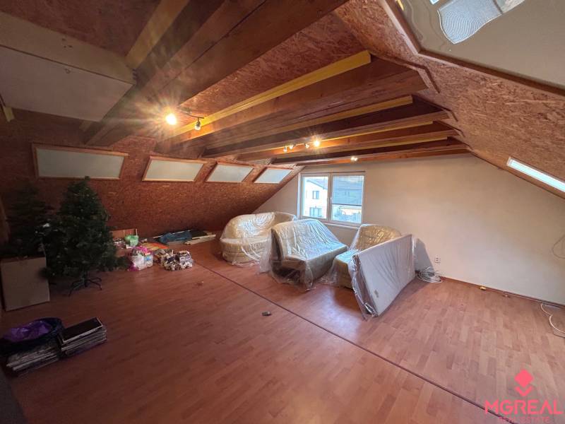 Podkrovní pokoj v rodinném domě s podlahou s dřevěným dekorem a střešními okny.