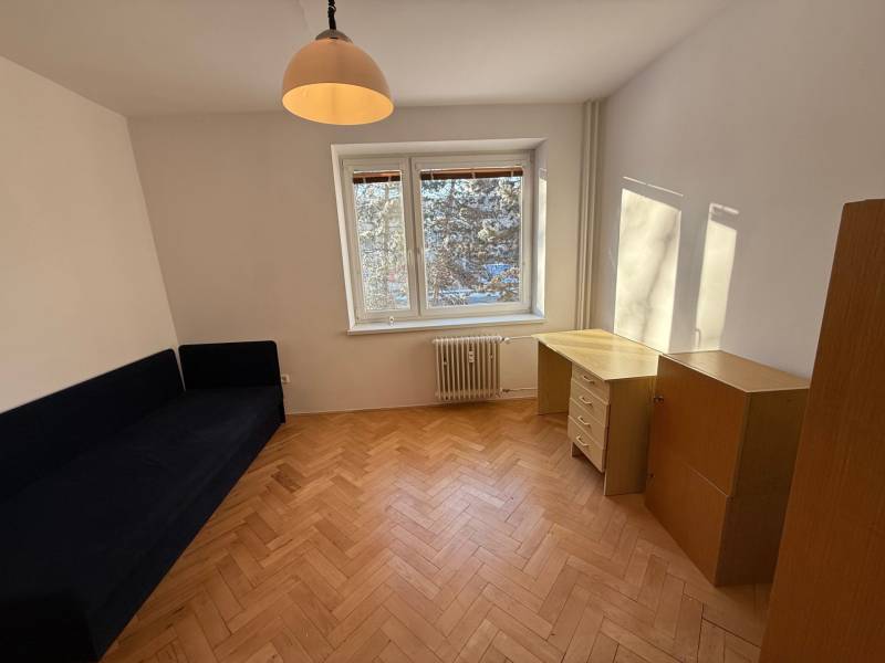 Pokoj v 3-pokojovém bytě s podlahou s dřevěným dekorem, modrou pohovkou a psacím stolem.