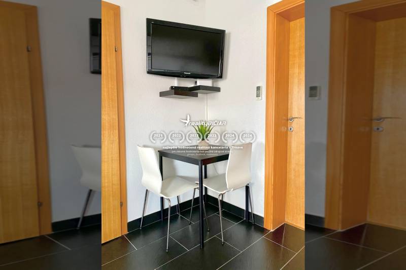 Jídelna v rodinném domě s rohovým stolem, televizorem na stěně a černými dlaždicemi.