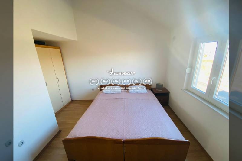 Ložnice v rodinném domě s postelí, nočním stolkem a podlahou s dřevěným dekorem.