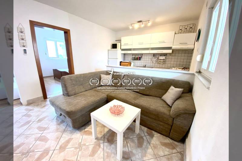 Interiér rodinného domu s pohovkou, bílým stolem a kuchyňským koutem.