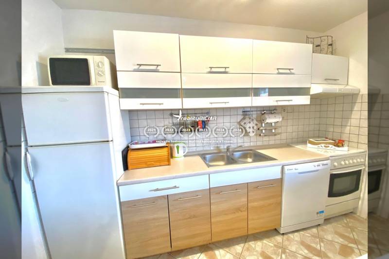 Kuchyně v rodinném domě s bílými skříňkami, sporákem a mikrovlnkou.