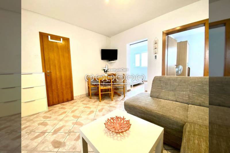 Obývací pokoj v rodinném domě s pohovkou, stolkem a televizí na stěně.