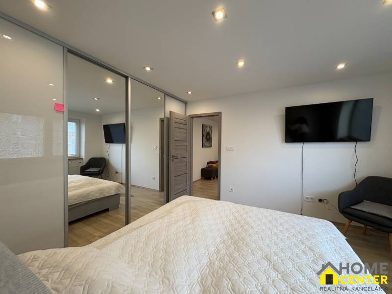 Ložnice v 2-pokojovém bytě s televizí, velkou skříní a podlahou s dřevěným dekorem.