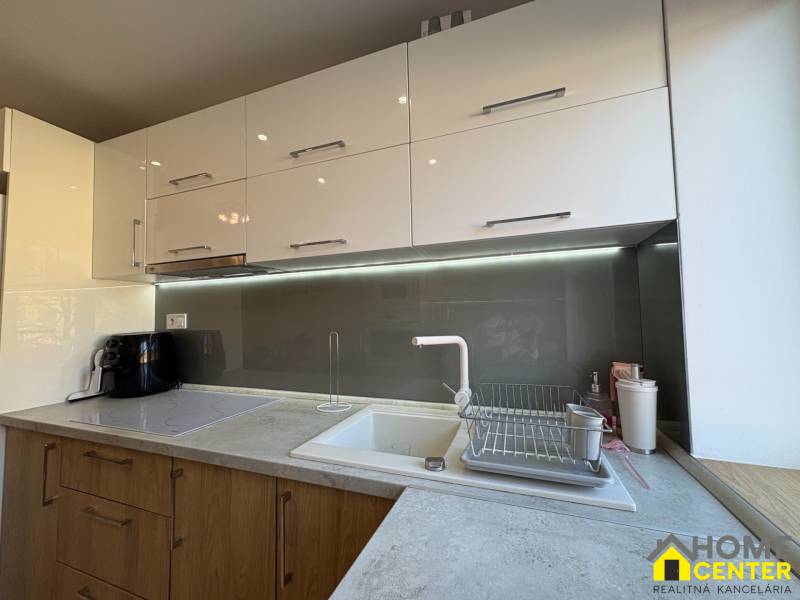 Kuchyně v 2pokojovém bytě se světlými skříňkami a podsvícením nad pracovní deskou.