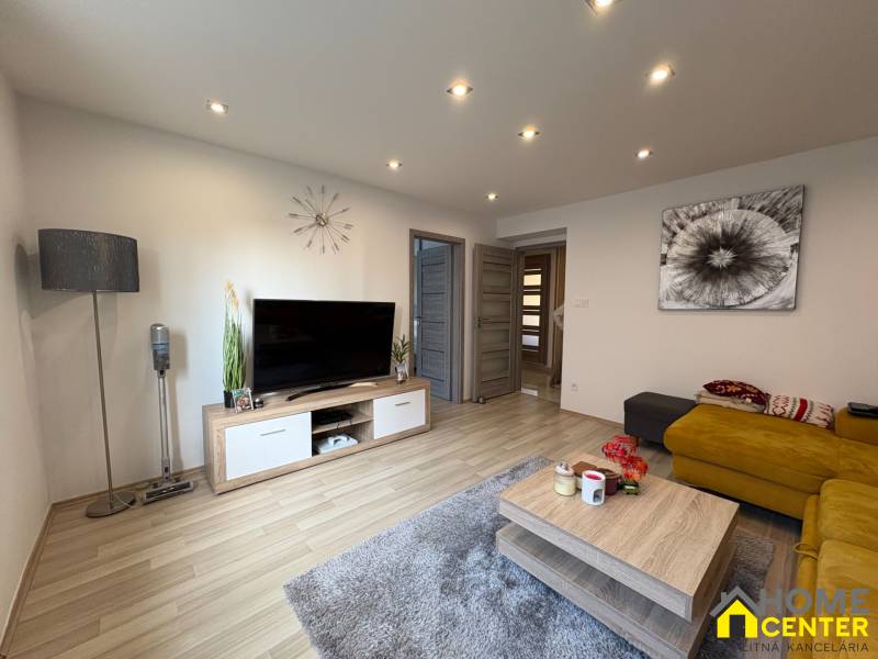 Obývací pokoj v 2-pokojovém bytě s podlahou s dřevěným dekorem, TV a žlutou pohovkou.