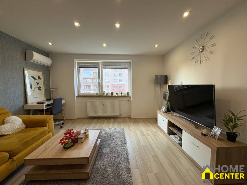 Obývací pokoj v 2-pokojovém bytě s podlahou s dřevěným dekorem, gaučem a televizorem.