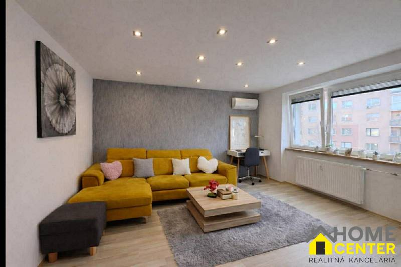 Obývací pokoj v 2-pokojovém bytě s pohovkou, podlaha s dřevěným dekorem, šedý koberec.