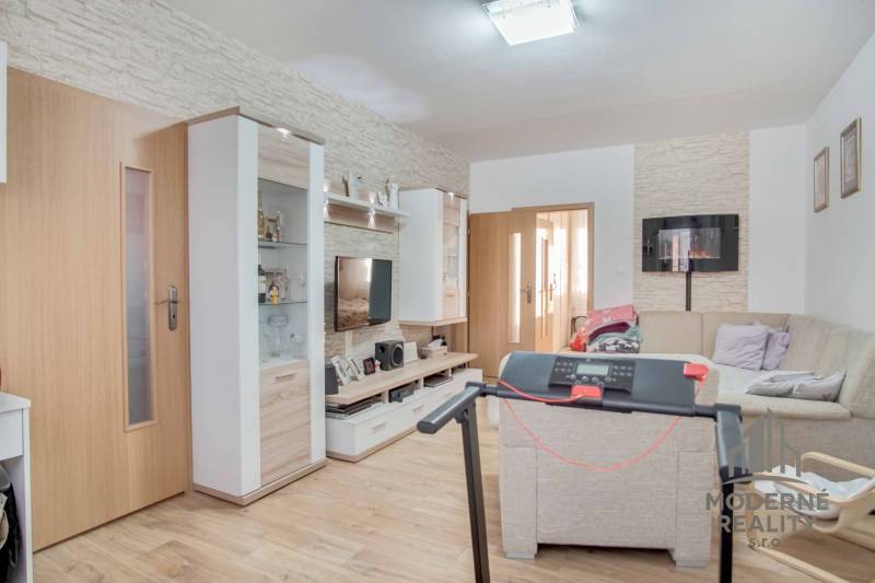 Obývací pokoj v 3pokojovém bytě s podlahou s dřevěným dekorem a rohovou sedačkou.