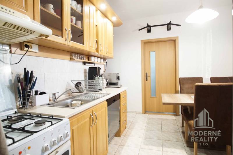 Kuchyně ve 3-pokojovém bytě s dřevěnými skříňkami a jídelním stolem.