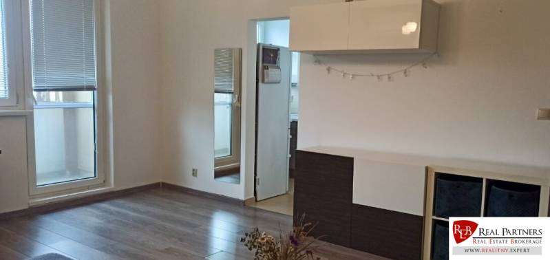 Obývací pokoj v 2pokojovém bytě s podlahou s dřevěným dekorem, bílým nábytkem a zrcadlem.