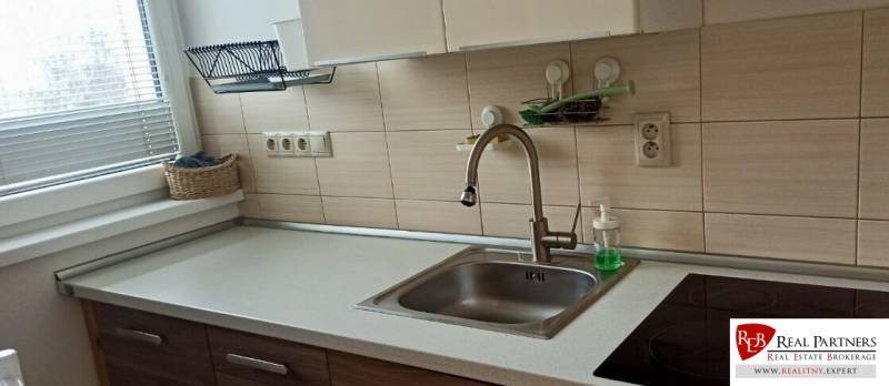 Kuchyně v 2-pokojovém bytě s dřezem, sklokeramickou varnou deskou a košíkem u okna.