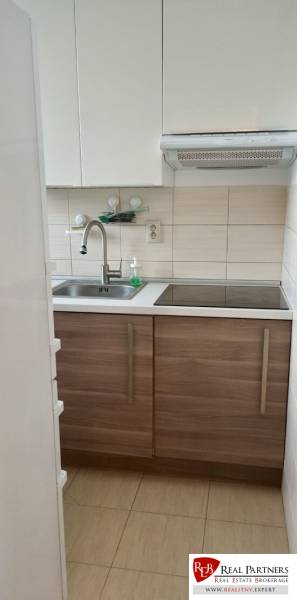 Kuchyně s bílými skříňkami a nerezovým dřezem v 2-pokojovém bytě.