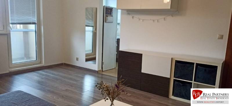 Obývací pokoj v 2pokojovém bytě s podlahou s dřevěným dekorem a vstupem na balkon.