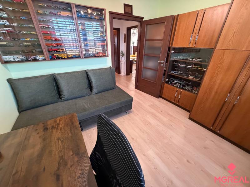 Pokoj s pohovkou, vitrínou s modely a podlahou s dřevěným dekorem v 3-pokojovém bytě.