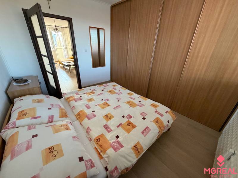 Ložnice v třípokojovém bytě s postelí, vestavěnou skříní a podlahou s dřevěným dekorem.