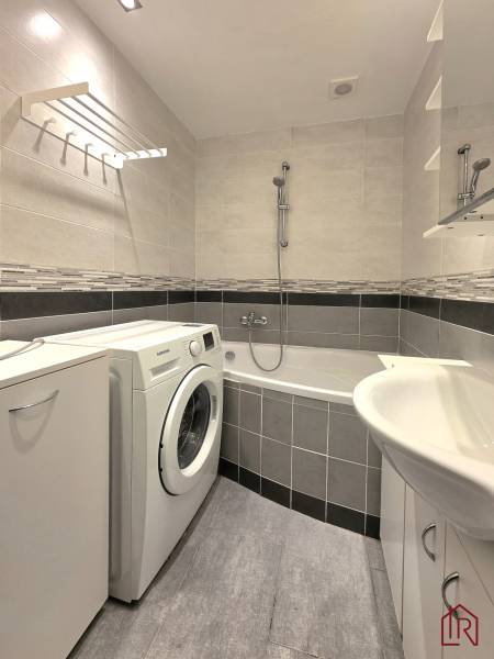 Koupelna s vanou, pračkou a dlažbou v 2-pokojovém bytě.