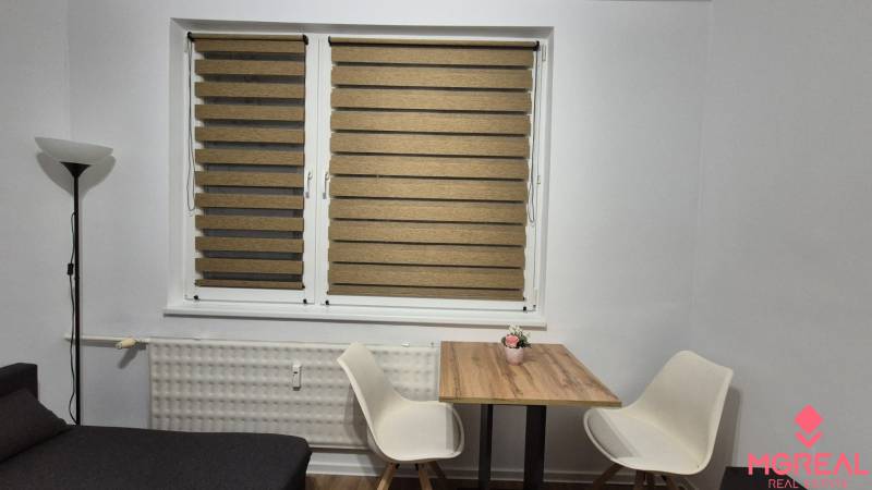 Jídelní kout s dřevěným stolkem a dvěma bílými židlemi v garsonce.