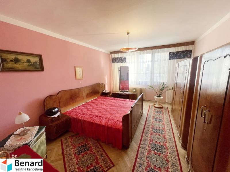 Ložnice ve 3pokojovém bytě s červenými doplňky a podlahou s dřevěným dekorem.