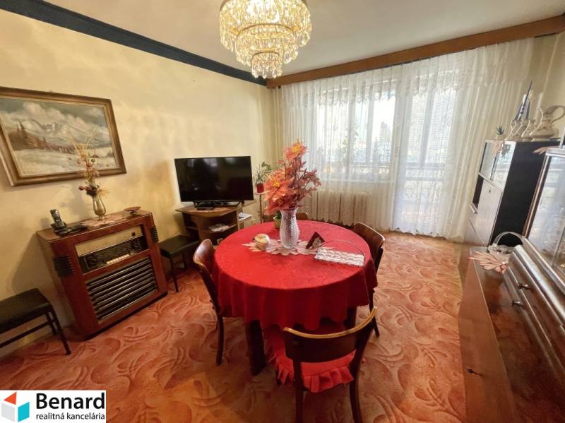 Jídelní část ve 3-pokojovém bytě s červeným ubrusem a velkými okny.