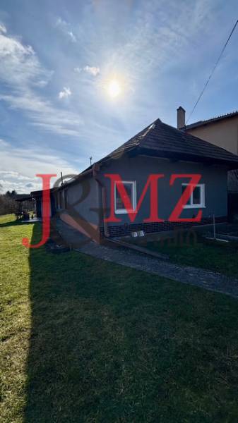 Rodinný dům v Mýtných Ludanech, obklopený zahradou, s modrou oblohou a sluncem.