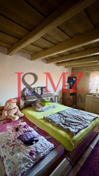 Ložnice v rodinném domě s dřevěným stropem, postelí a plyšovým medvědem.