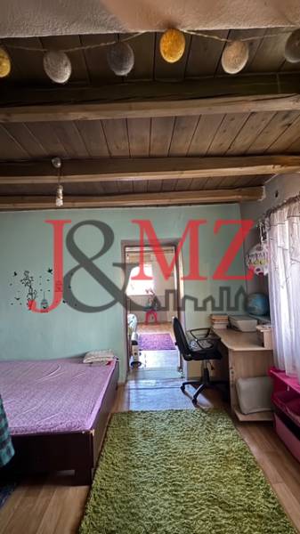 Pokoj s podlahou s dřevěným dekorem, postelí, pracovním stolem a dekoračními trámy na stropě.