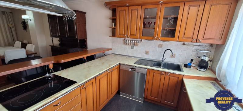 Kuchyně v rodinném domě s dřevěnými skříňkami a nerezovou myčkou nádobí.