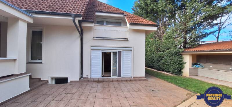 Rodinný dům v Komárně s terasou, zahradou a bílými okenicemi.