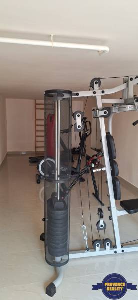 Fitness místnost s posilovacími stroji v rodinném domě má světlý keramický povrch.