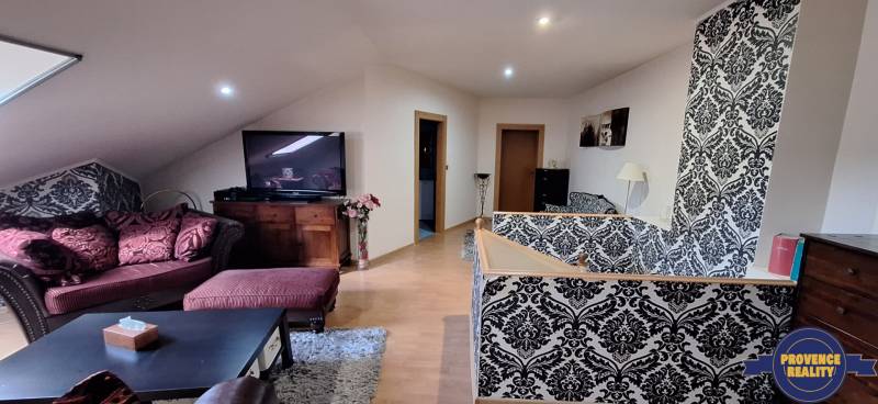 Obývací pokoj v rodinném domě s pohovkou, vzorovanou tapetou a televizí.