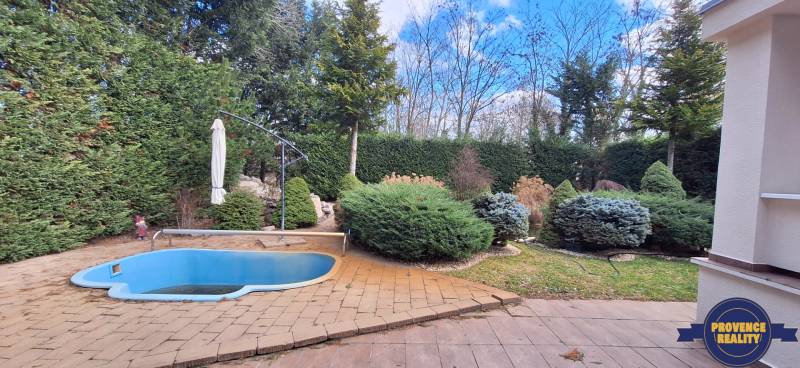 Rodinný dům v Komárně s malým bazénem a udržovanou zahradou obklopenou stromy.