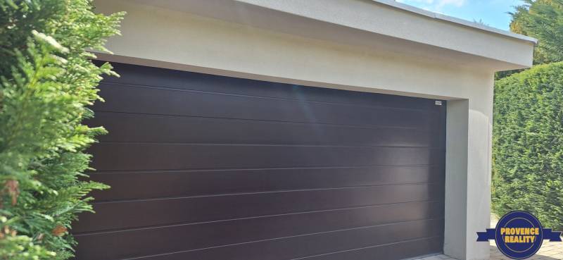 Garážová vrata u rodinného domu v Komárně, obklopená zelení.