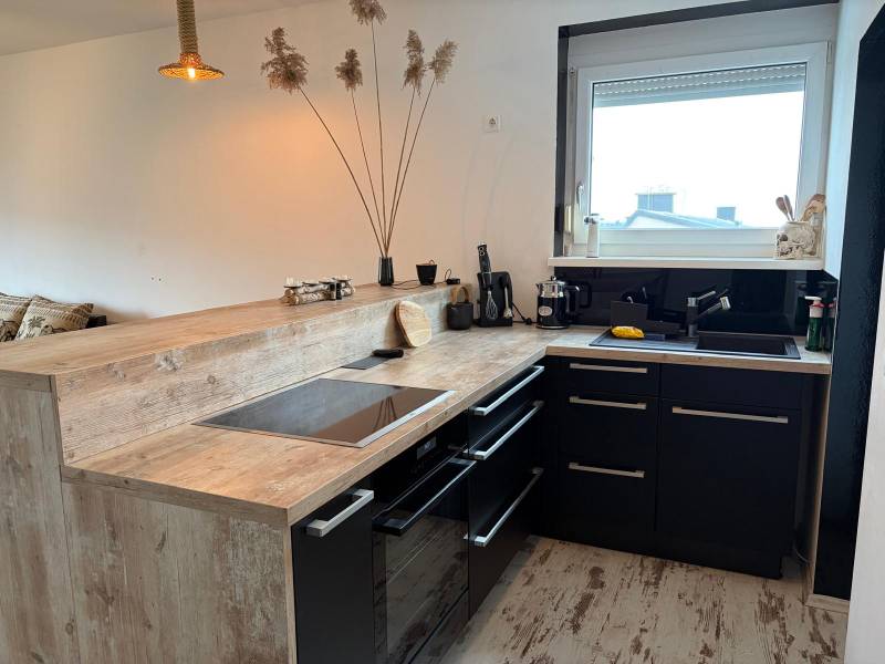 Kuchyně ve 3-pokojovém bytě s černými skříňkami a podlahou s dřevěným dekorem.