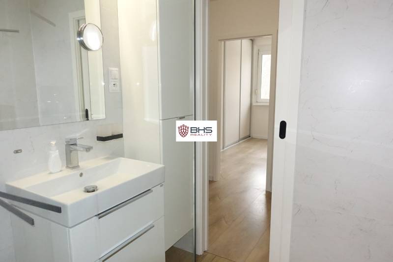 Koupelna s umyvadlem, bílou skříňkou a výhledem do chodby ve 3-pokojovém bytě.