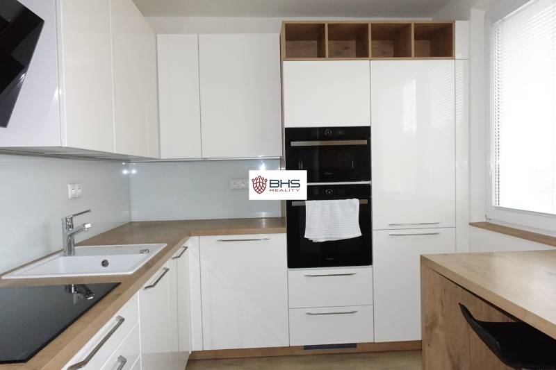 Moderní kuchyně s bílými skříňkami a podlahou s dřevěným dekorem v 3pokojovém bytě.