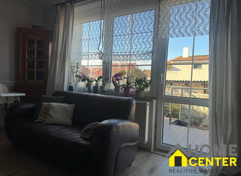 Kožená sedačka a okno s krajkovými závěsy v rodinném domě s podlahou s dřevěným dekorem.