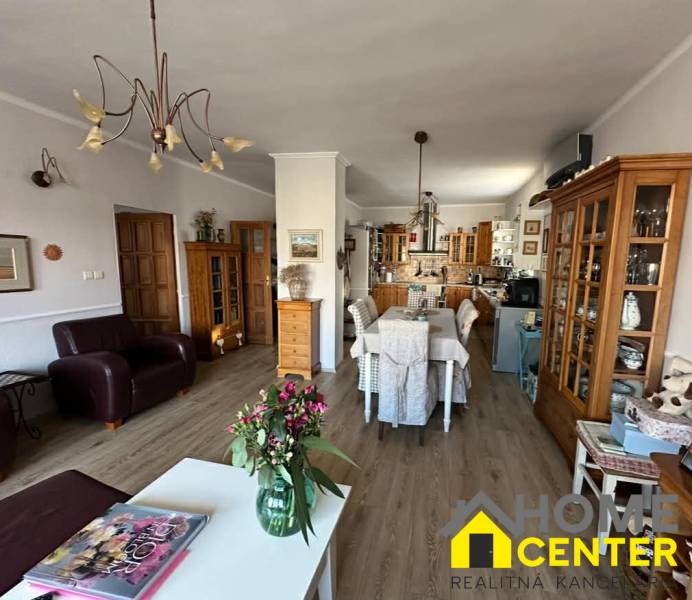 Obývací pokoj s kuchyní v rodinném domě, podlaha s dřevěným dekorem, květiny na stole.