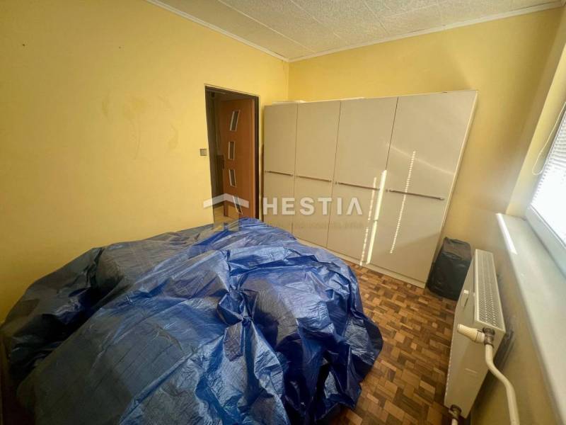 Pokoj se skříní, radiátorem a zakrytým nábytkem ve 3-pokojovém bytě.