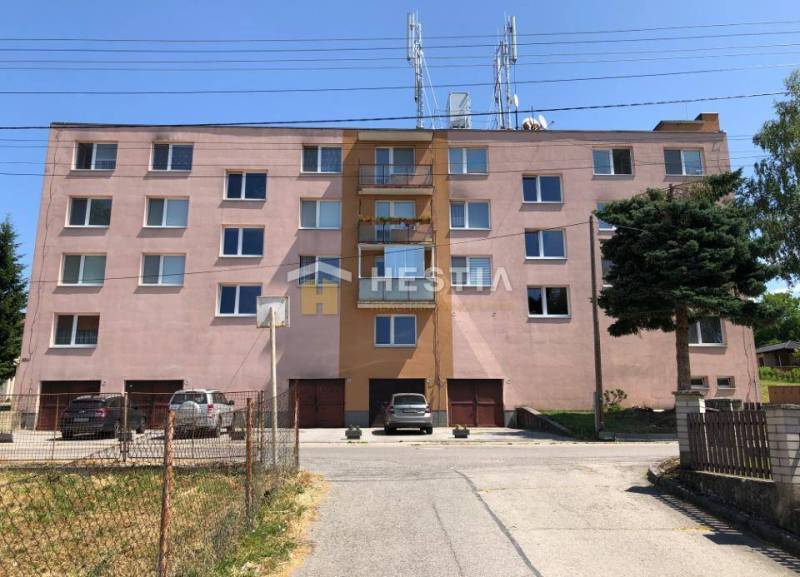 Bytový dům v Moravském Lieskovém s parkováním a přítomností velkého stromu v popředí.