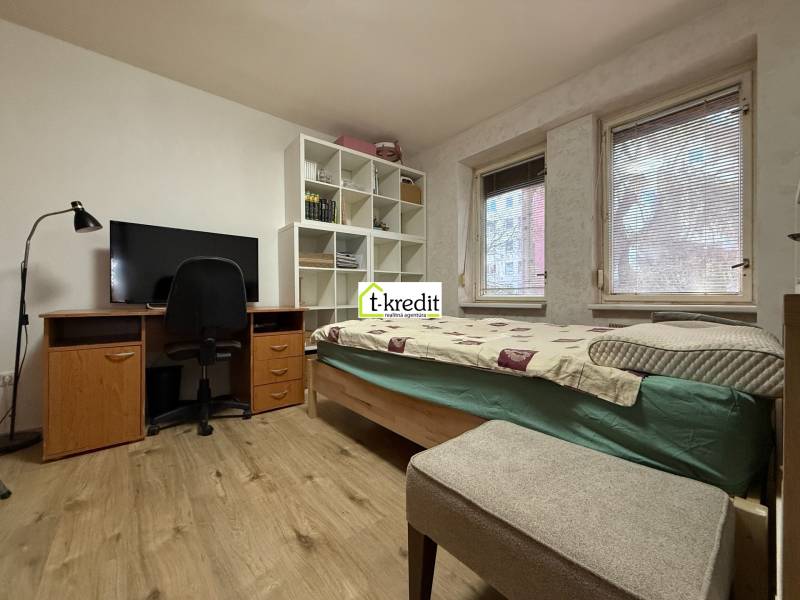 Pokoj v 2-pokojovém bytě s postelí, pracovním stolem a podlahou s dřevěným dekorem.