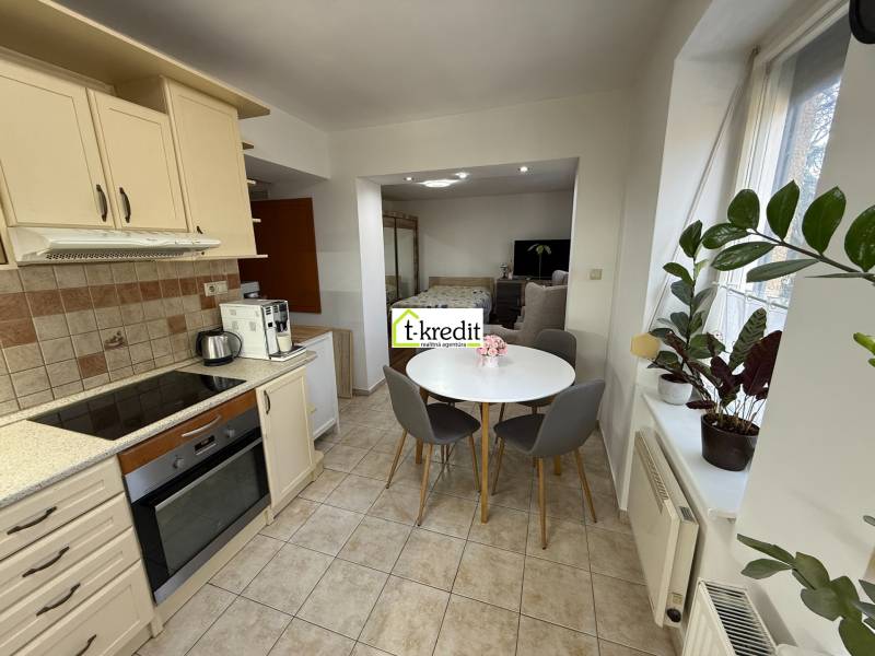 Kuchyně v 2-pokojovém bytě s kulatým stolem, rostlinami a spotřebiči.