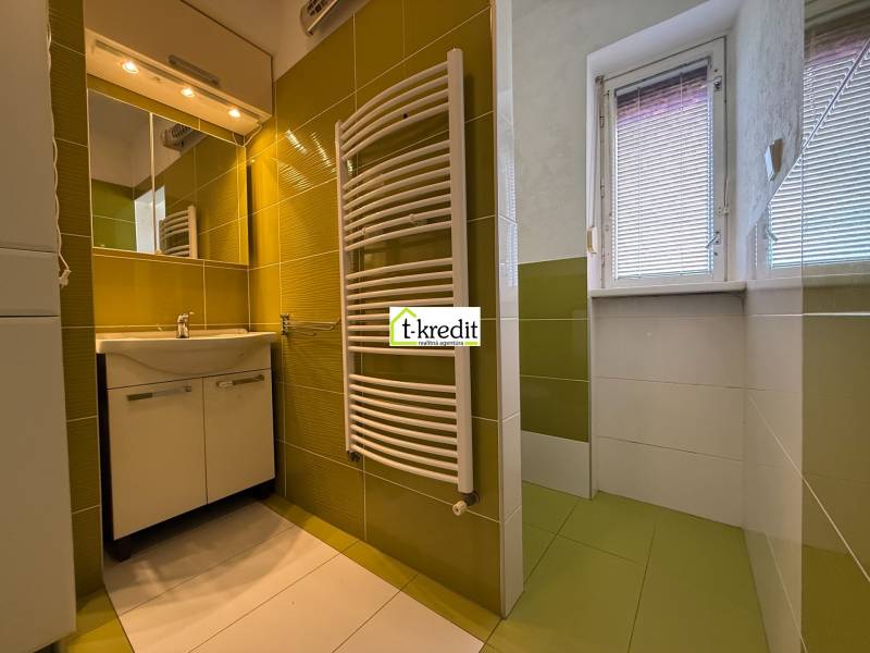 Koupelna v 2-pokojovém bytě s umyvadlem, zrcadlem a zeleno-bílými obklady.