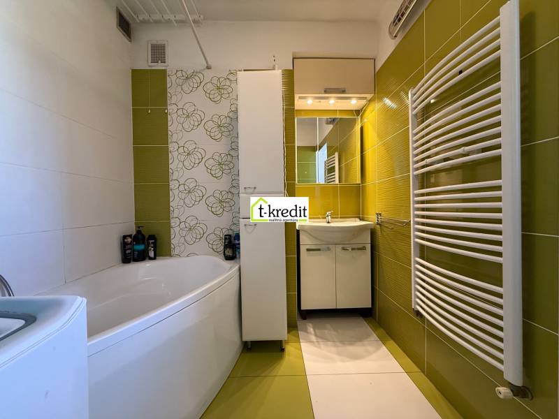 Koupelna v 2-pokojovém bytě se zelenými obklady, vanou a moderním topným tělesem.