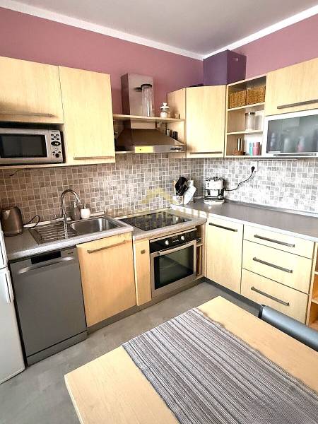 Kuchyně v 3pokojovém bytě s dřevěným dekorem skříněk, sušičkou a troubou.