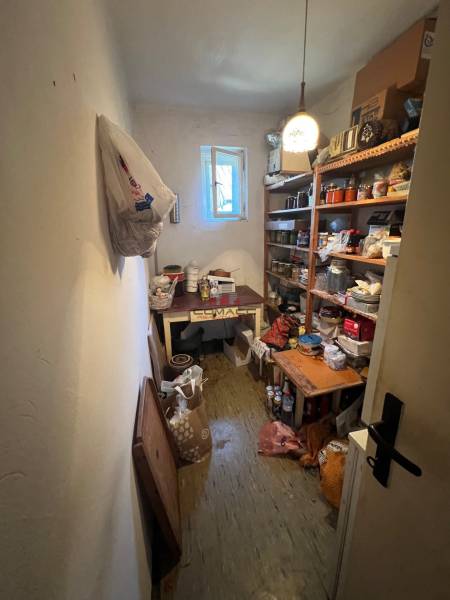 Úložný prostor v rodinném domě s regály plnými různých předmětů a otevřeným oknem.