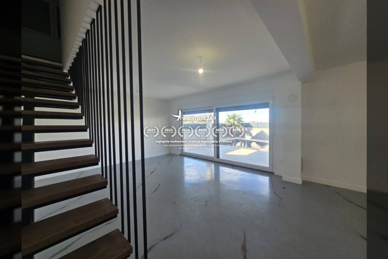 Obývací pokoj ve vile s moderním schodištěm a velkými okny.