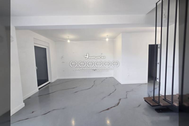 Prostorná místnost ve vile s bílými stěnami a šedou podlahou s dekorem.