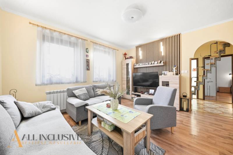 Obývací pokoj v rodinném domě s pohovkou, stolkem, televizí a podlahou s dřevěným dekorem.